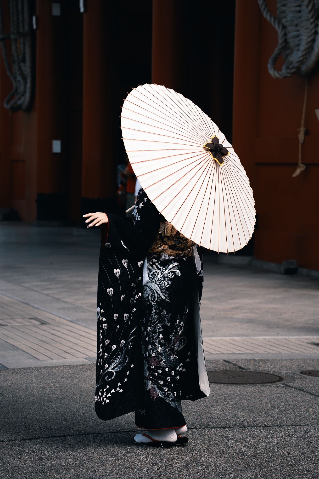 A person in a black kimono holding a white paper wagasa umbrella in Asakusa, Tokyo