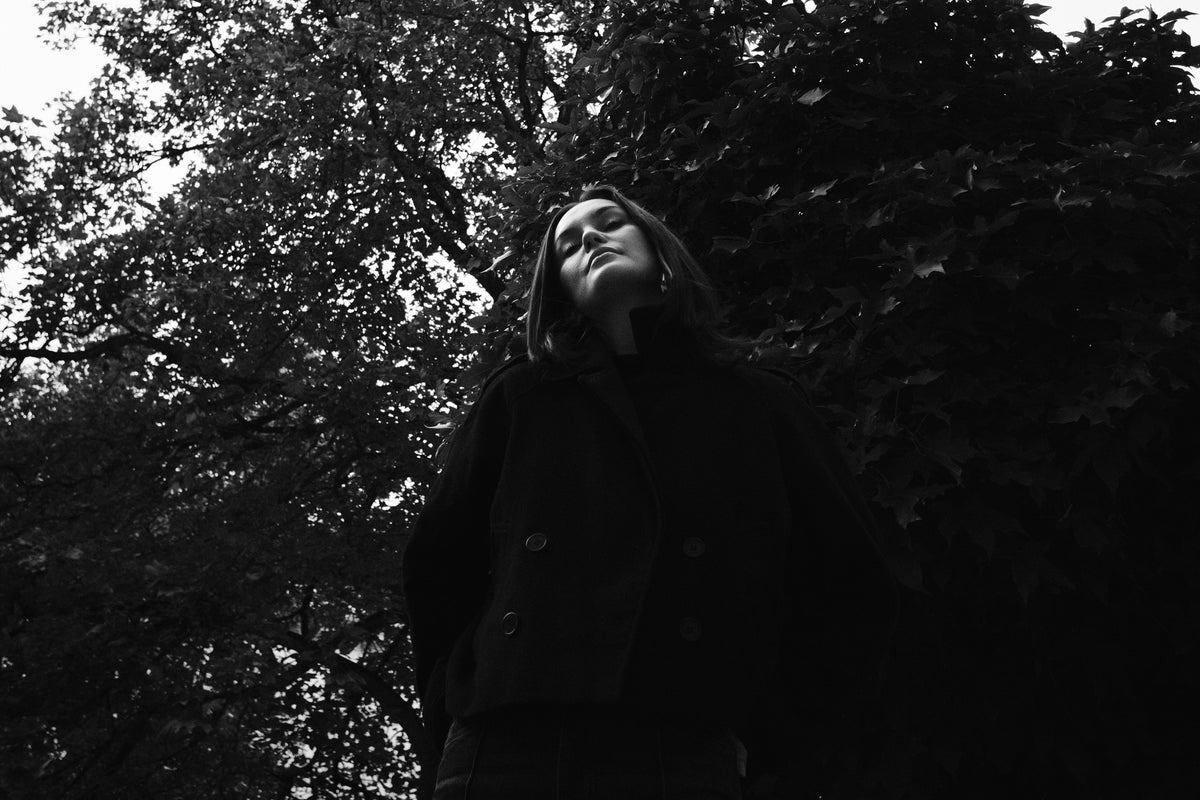 Helena Wedekind photographed from below against dark trees, eyes closed