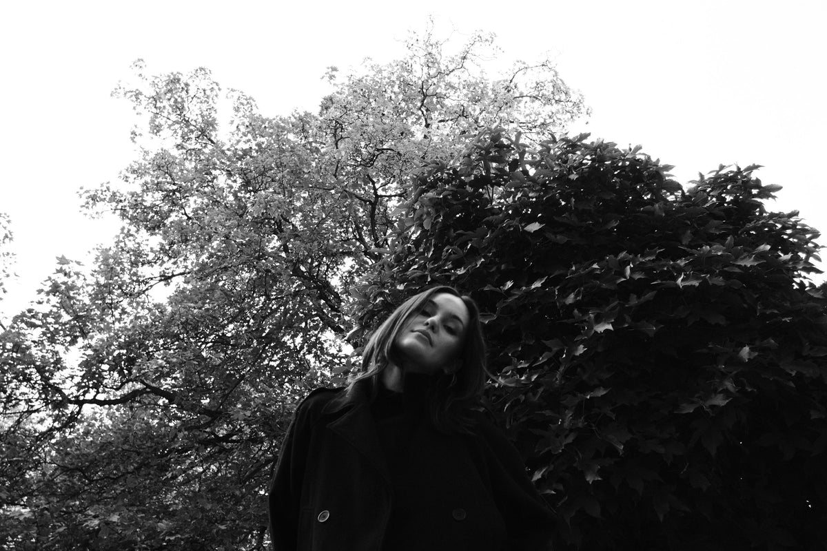 Helena Wedekind from below, head tilted back, framed by trees against a white sky