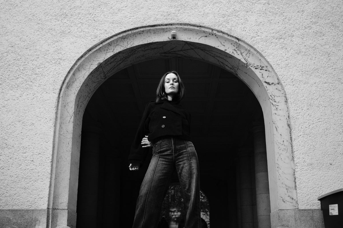 Helena Wedekind standing in a stone archway, one hand at her collar