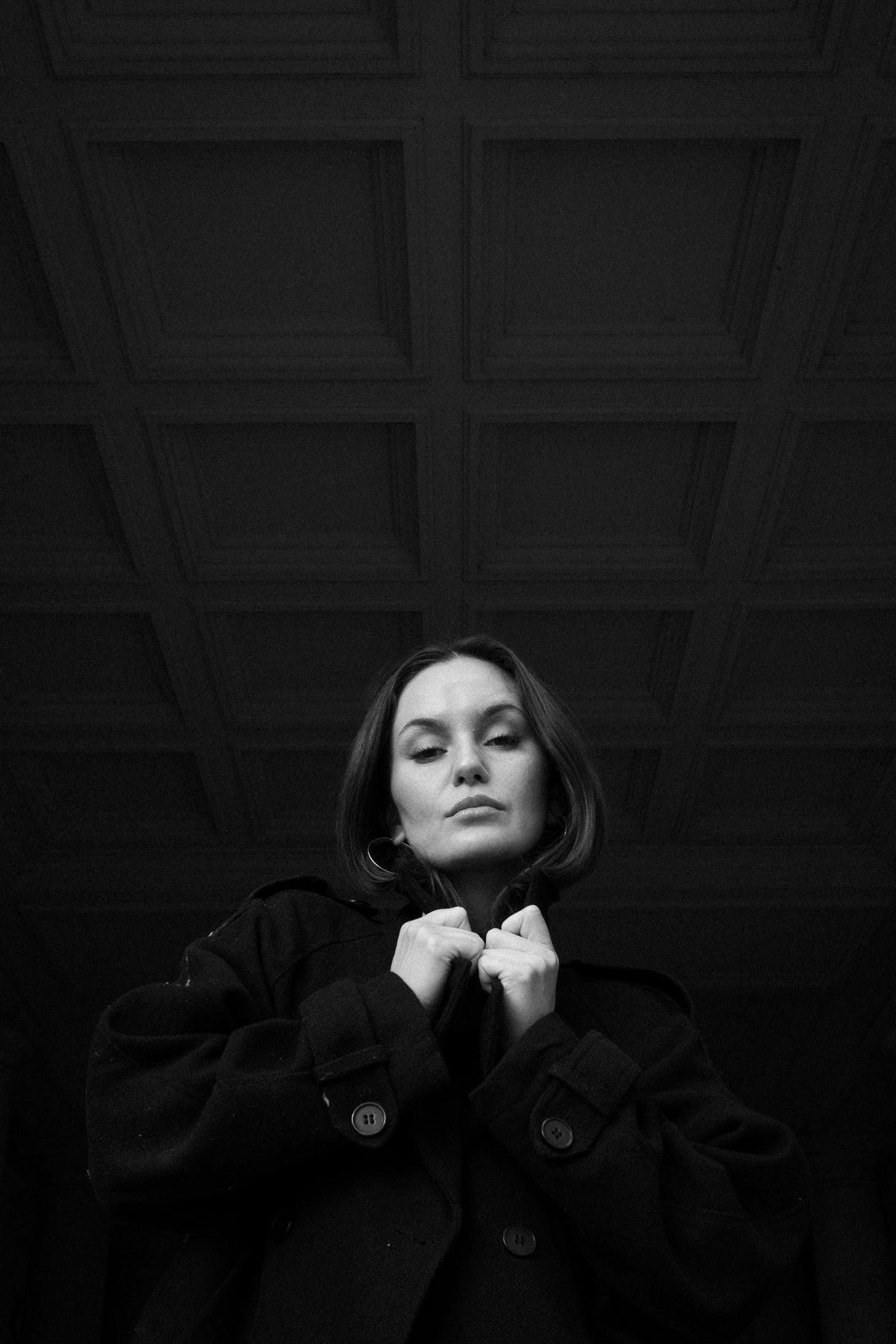 Helena Wedekind under a coffered ceiling, gripping the collar of her coat