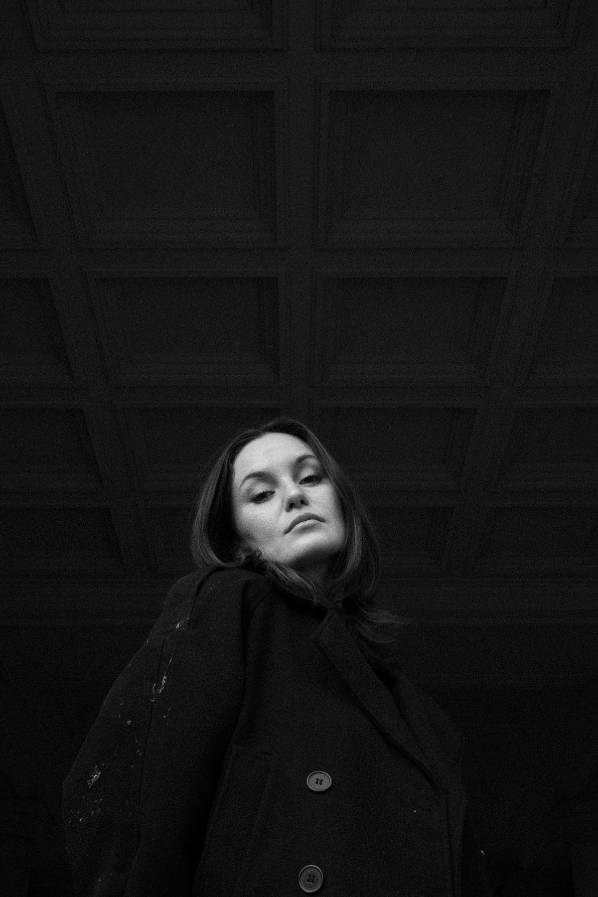 Helena Wedekind under a coffered ceiling, head tilted, looking down at the camera