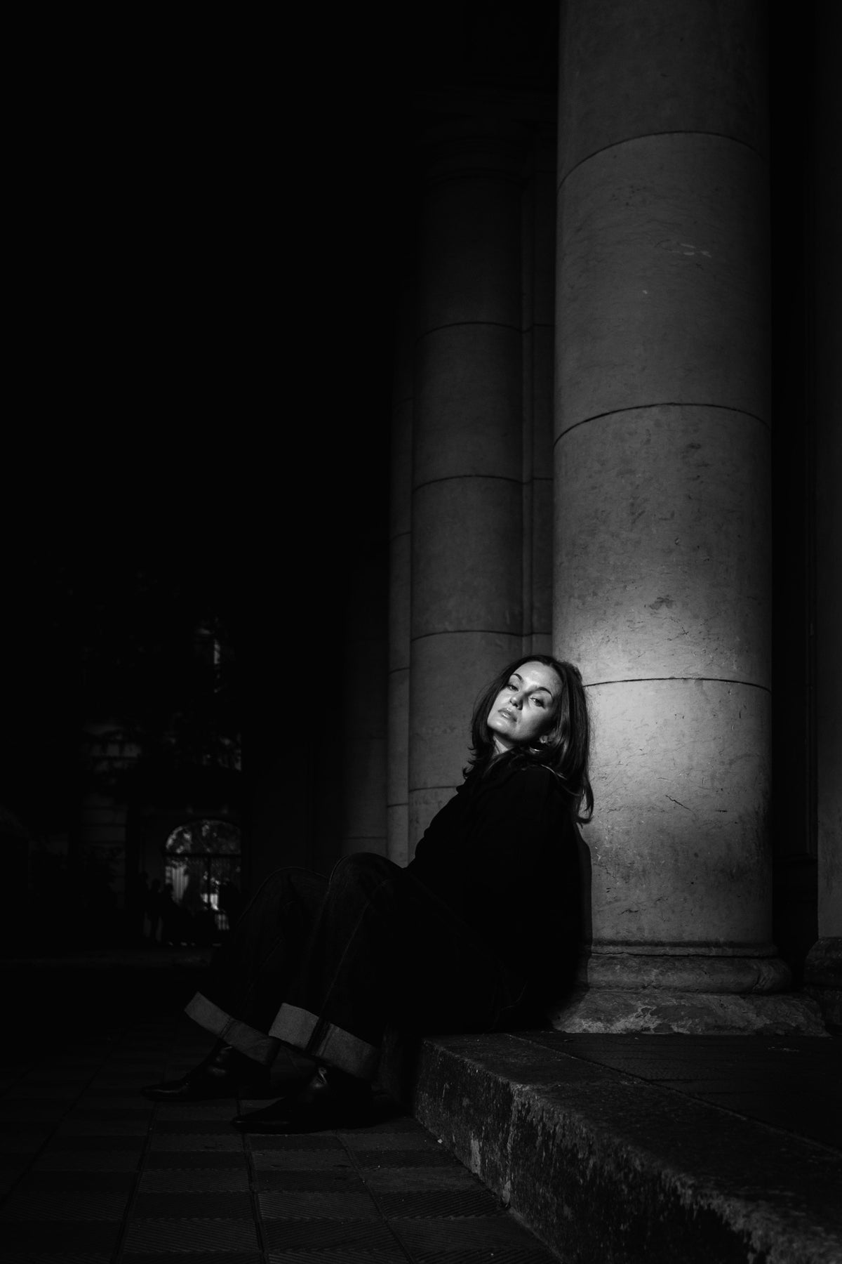 Helena Wedekind sitting against a lit stone column in deep shadow