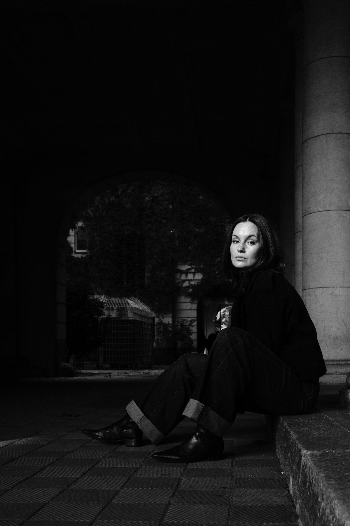 Helena Wedekind seated on a stone ledge by an archway, looking at the camera