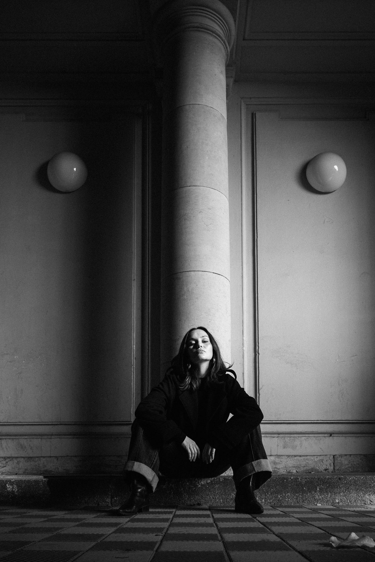 Helena Wedekind crouched against a column between two globe lamps, looking at the camera