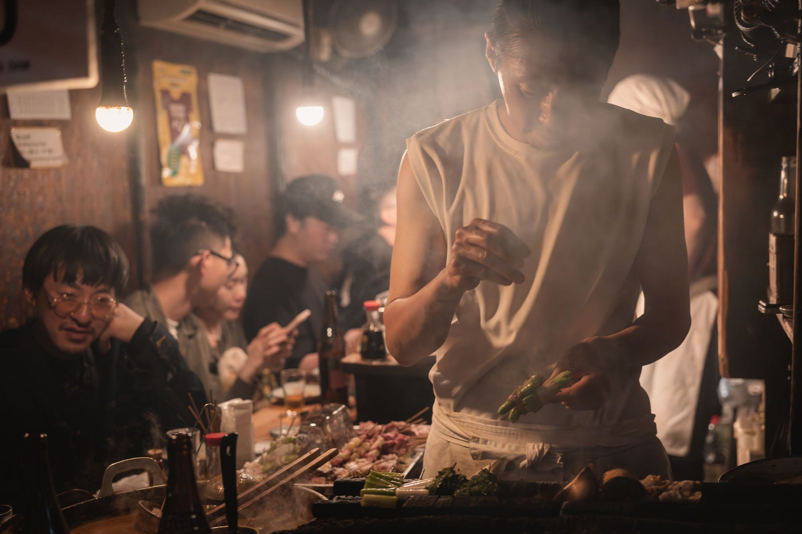A cook grilling skewers inside a small izakaya in Omoide Yokocho, Tokyo at night