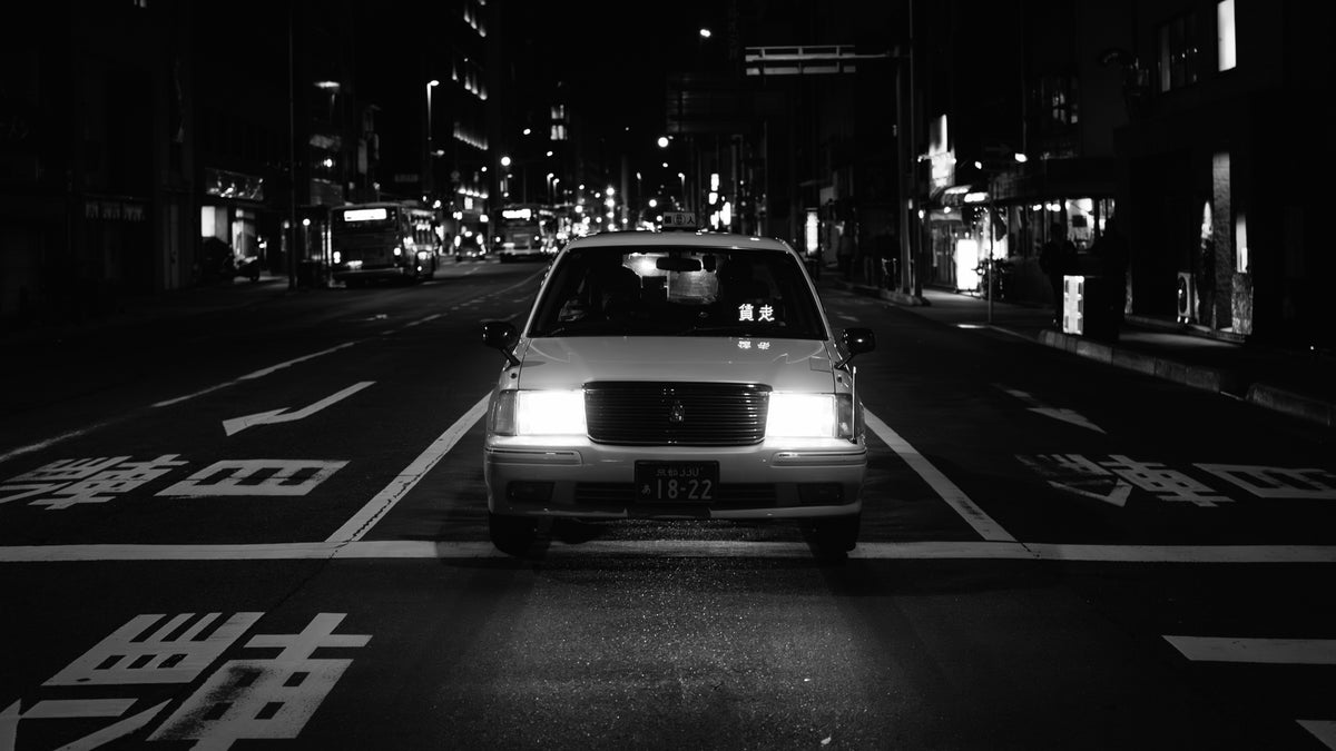 White taxi head-on on a night road, headlights on